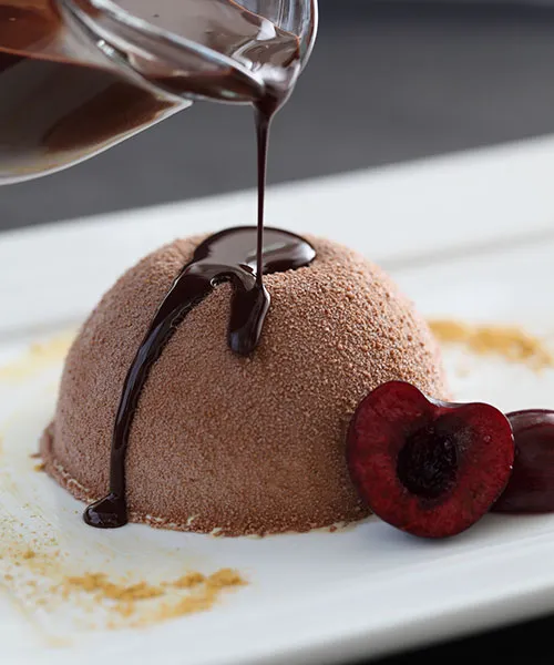 A chocolate gelato dome with sauce and a cherry
